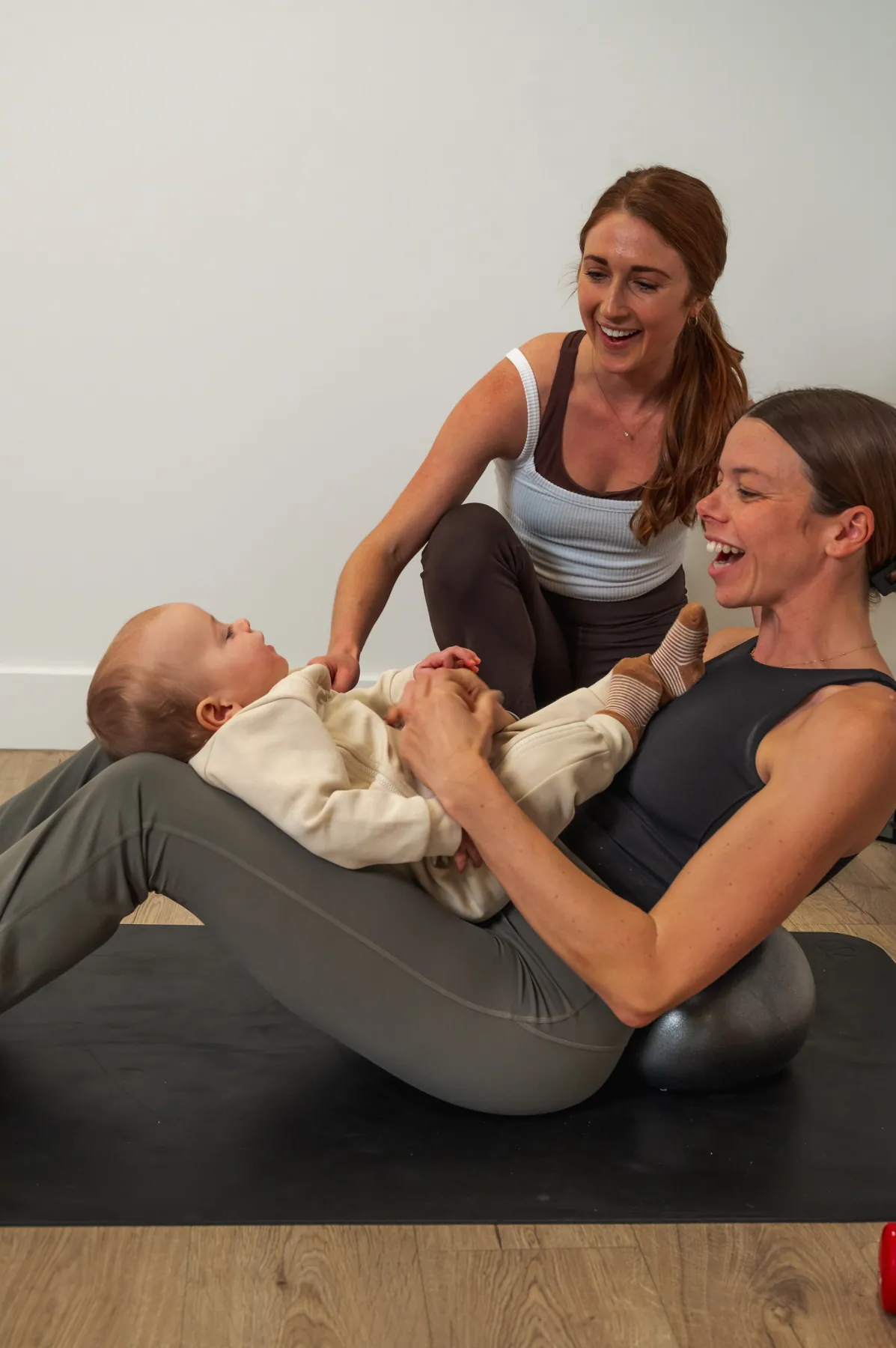 A new mum laughing with her baby on her lap during a class with Bridget
